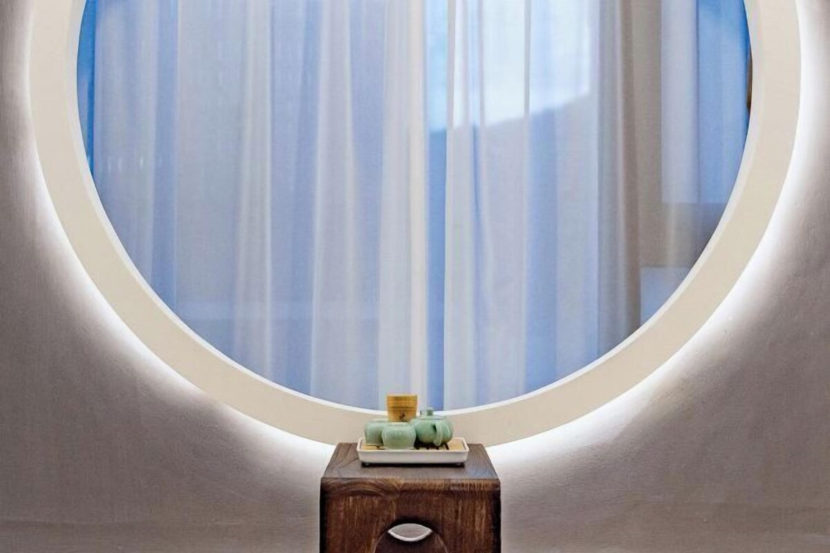 A room with a round window, a wooden side table with a small decorative item, and sheer curtains.