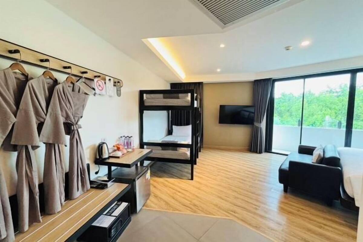 Une chambre d’hôtel avec un lit superposé, un coin salon avec une table et des chaises, un téléviseur fixé au mur et une grande fenêtre donnant sur un paysage verdoyant.