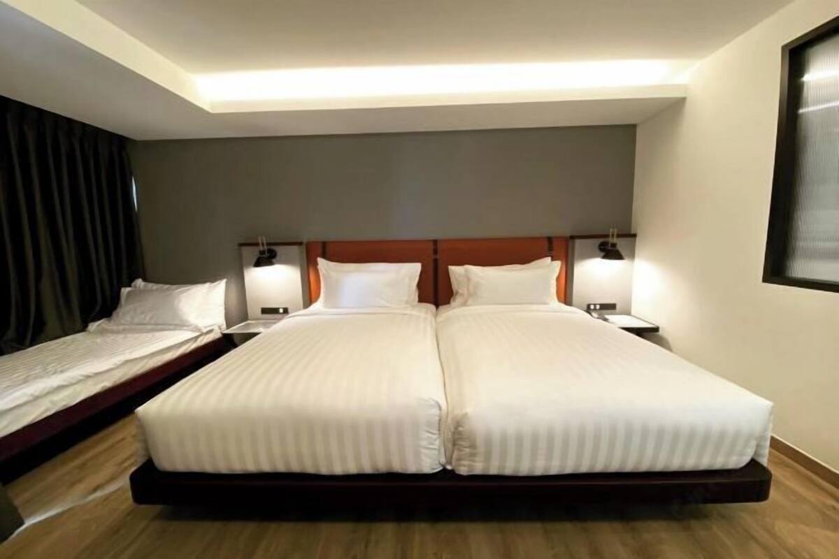 Une chambre d’hôtel avec un lit double, un lit simple et une table de chevet avec une lampe.
