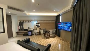 A hotel room with a bed, a desk with a chair, a TV, and a seating area.