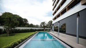 Une piscine rectangulaire bordée d’une terrasse carrelée, entourée d’une pelouse bien entretenue et d’arbres.