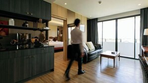 Une chambre d’hôtel moderne avec un plancher en bois, un canapé, une petite table, un coin cuisine avec des placards et une grande fenêtre offrant une vue.