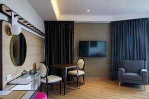 Ein Hotelzimmer mit Holzboden, einem Schreibtisch mit Stuhl, einem an der Wand montierten Fernseher und einer Couch.