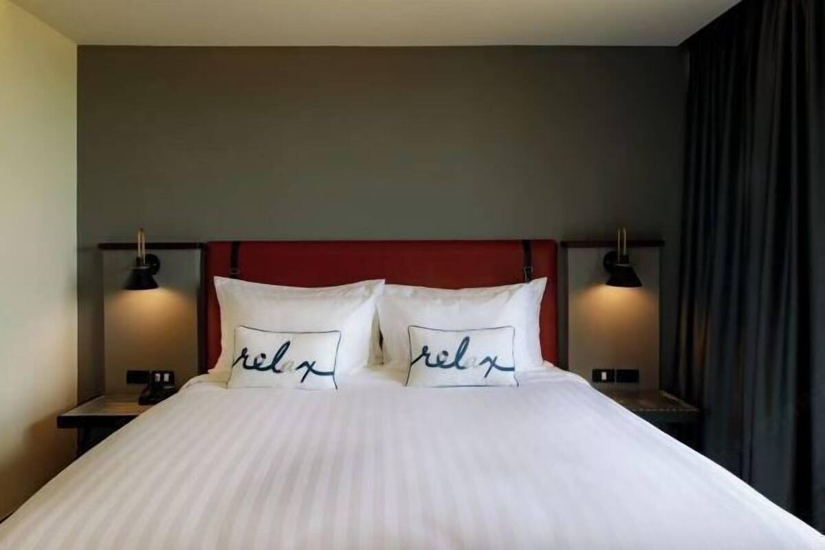 Une chambre d’hôtel avec un lit, deux lampes de chevet et une tête de lit rouge.