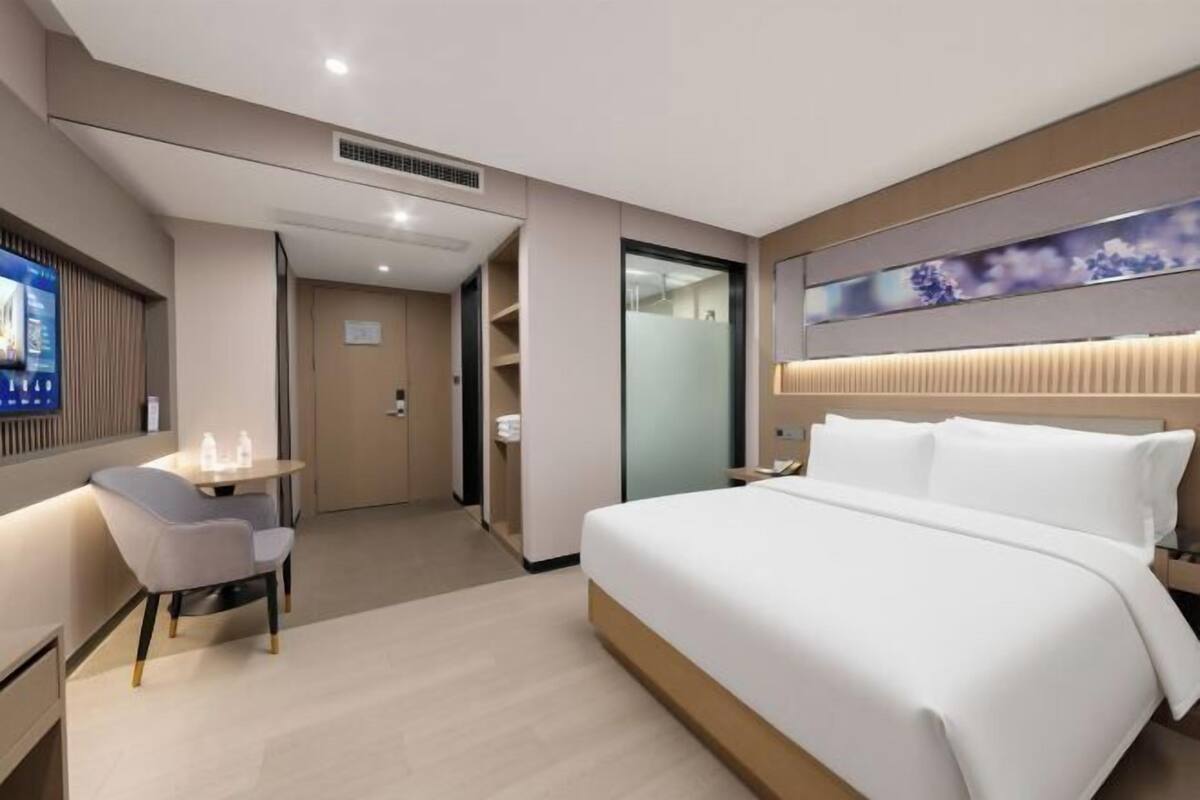 Ein modernes Hotelzimmer mit Bett, Nachttisch, Sessel und Fernseher.