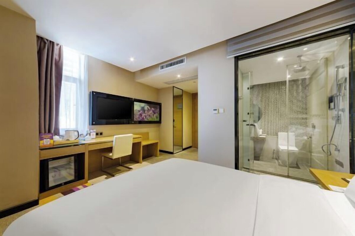 A hotel room with a bed, a desk with a computer, a TV, and a shower area.
