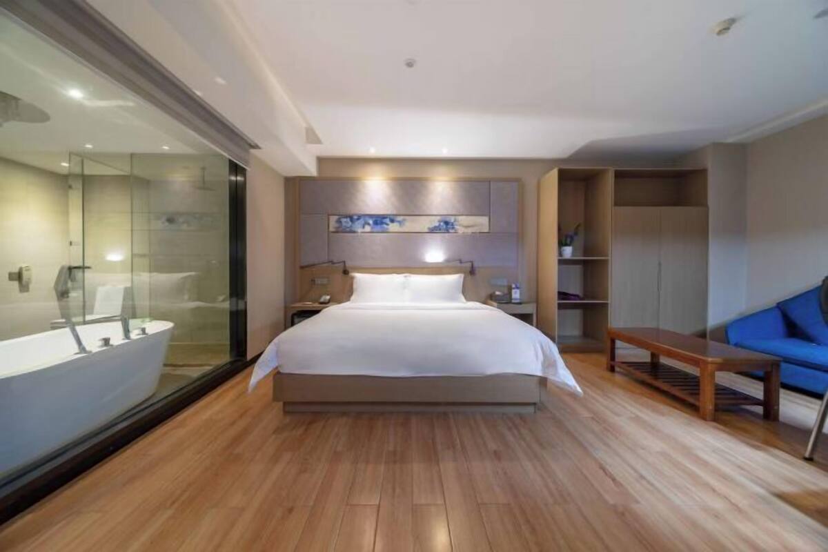 Ein modernes Schlafzimmer mit einem großen Bett, einer Duschkabine aus Glas, Holzboden, einem blauen Sofa und einem Einbauschrank.