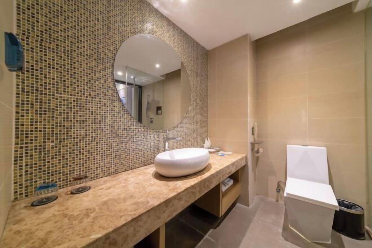 A bathroom with a mosaic tile wall, a round mirror, a white sink, and a white toilet.