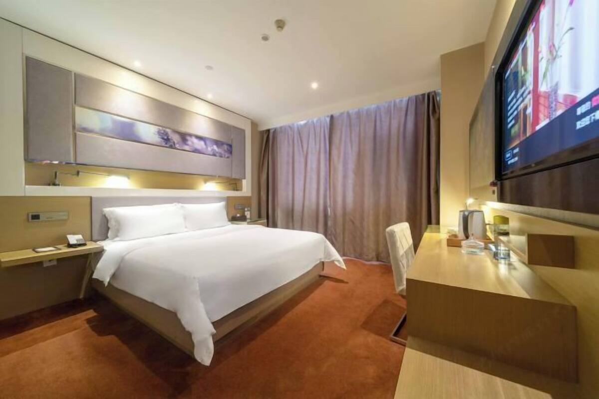Ein Hotelzimmer mit Bett, Schreibtisch, Fernseher und einem großen Fenster mit Vorhängen.