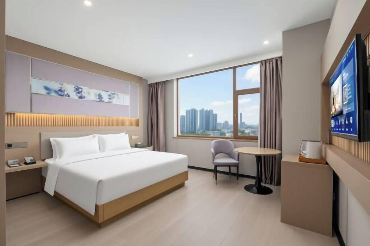 Ein Hotelzimmer mit Bett, Schreibtisch, Stuhl, Fernseher und einem Fenster mit Blick auf die Stadt.