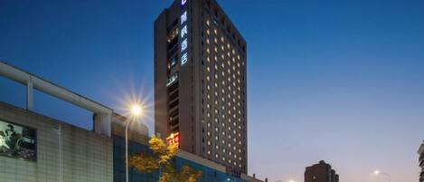 A high-rise hotel with a prominent 'L' logo, surrounded by a busy urban street at dusk.