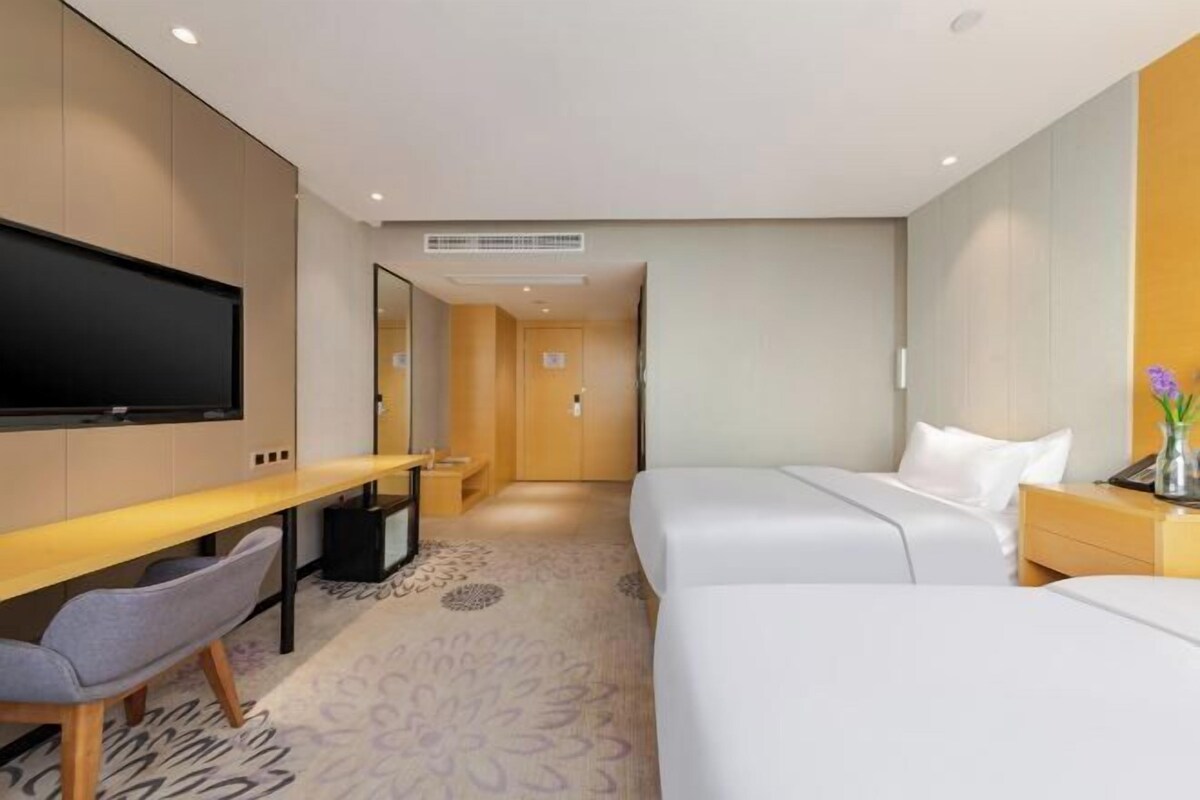 A hotel room with a bed, a desk, a chair, a TV, and a mirror.