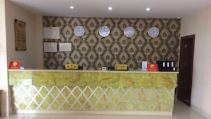 Un mostrador de recepción con un papel tapiz estampado, relojes, diplomas enmarcados y un pequeño letrero.
