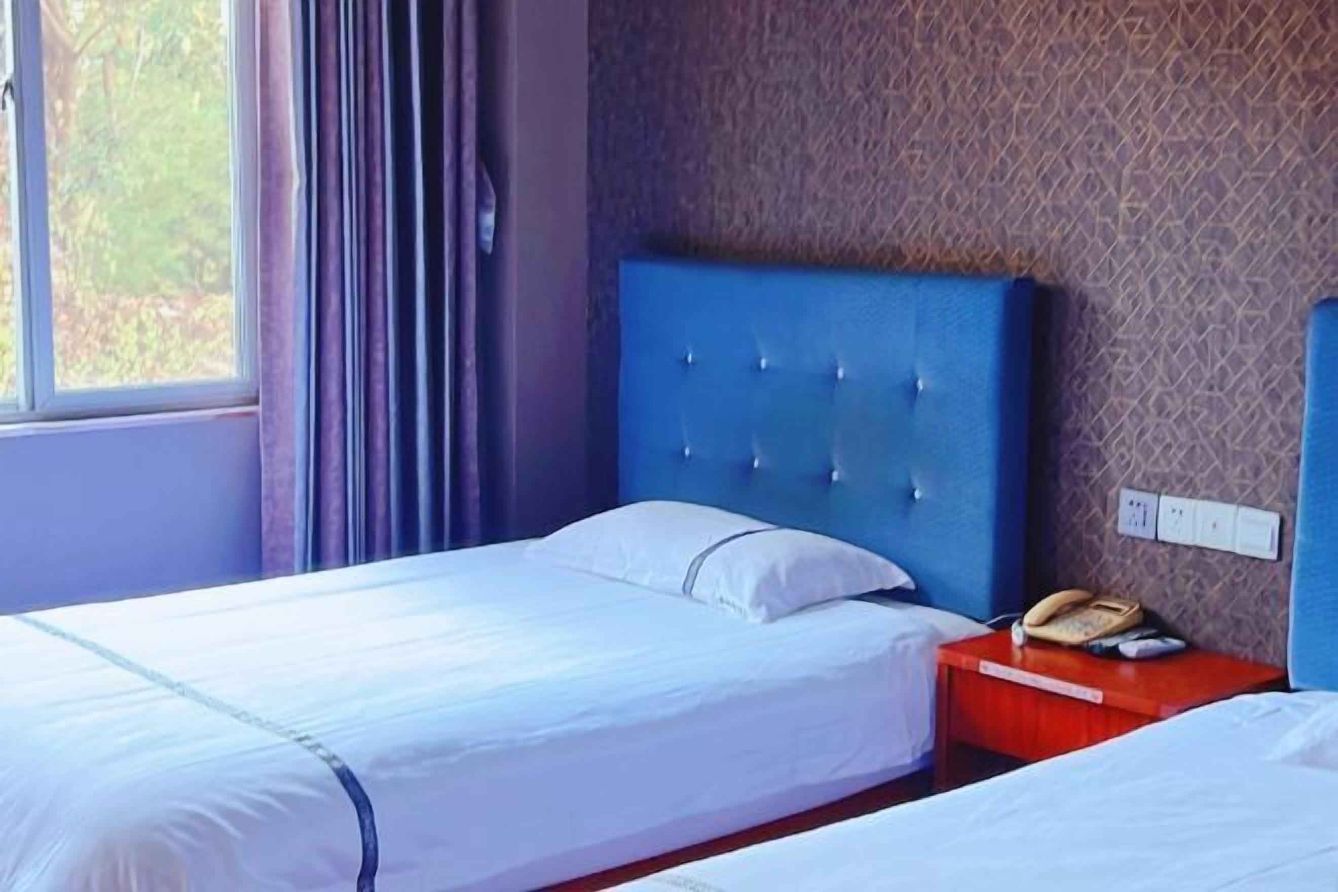 Une chambre d’hôtel avec deux lits, un téléphone sur la table de chevet et une fenêtre avec des rideaux.