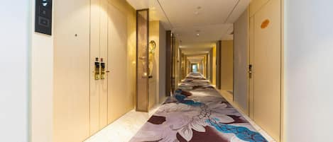 A hotel hallway with a patterned carpet, wooden doors, and a light-colored floor.