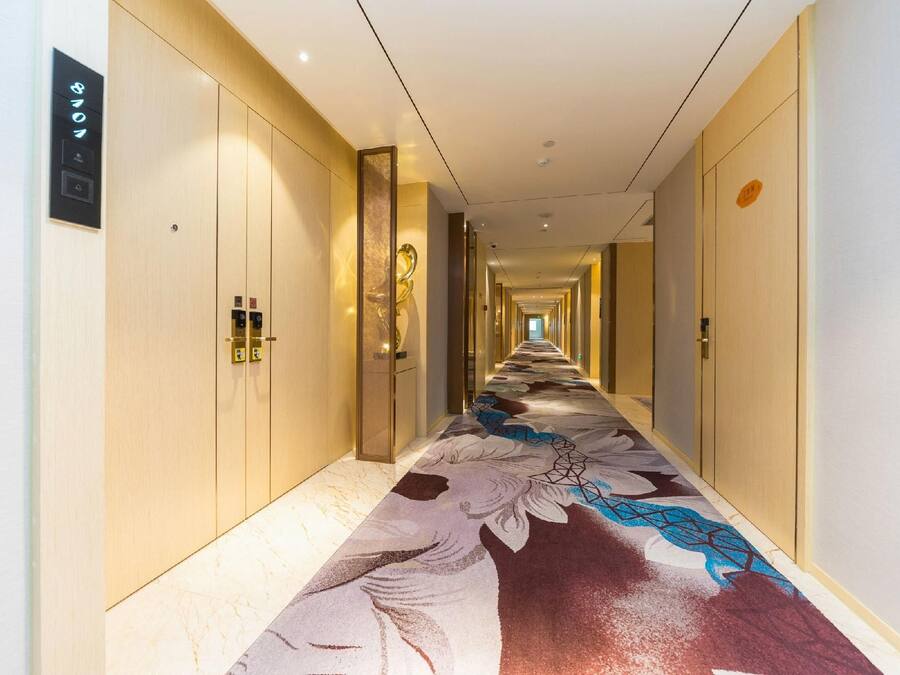 A hotel hallway with a patterned carpet, wooden doors, and a light-colored floor.