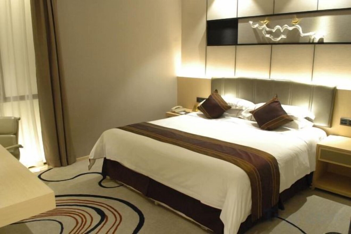 Una habitación de hotel con una cama grande, mesitas de noche, un escritorio y una silla.