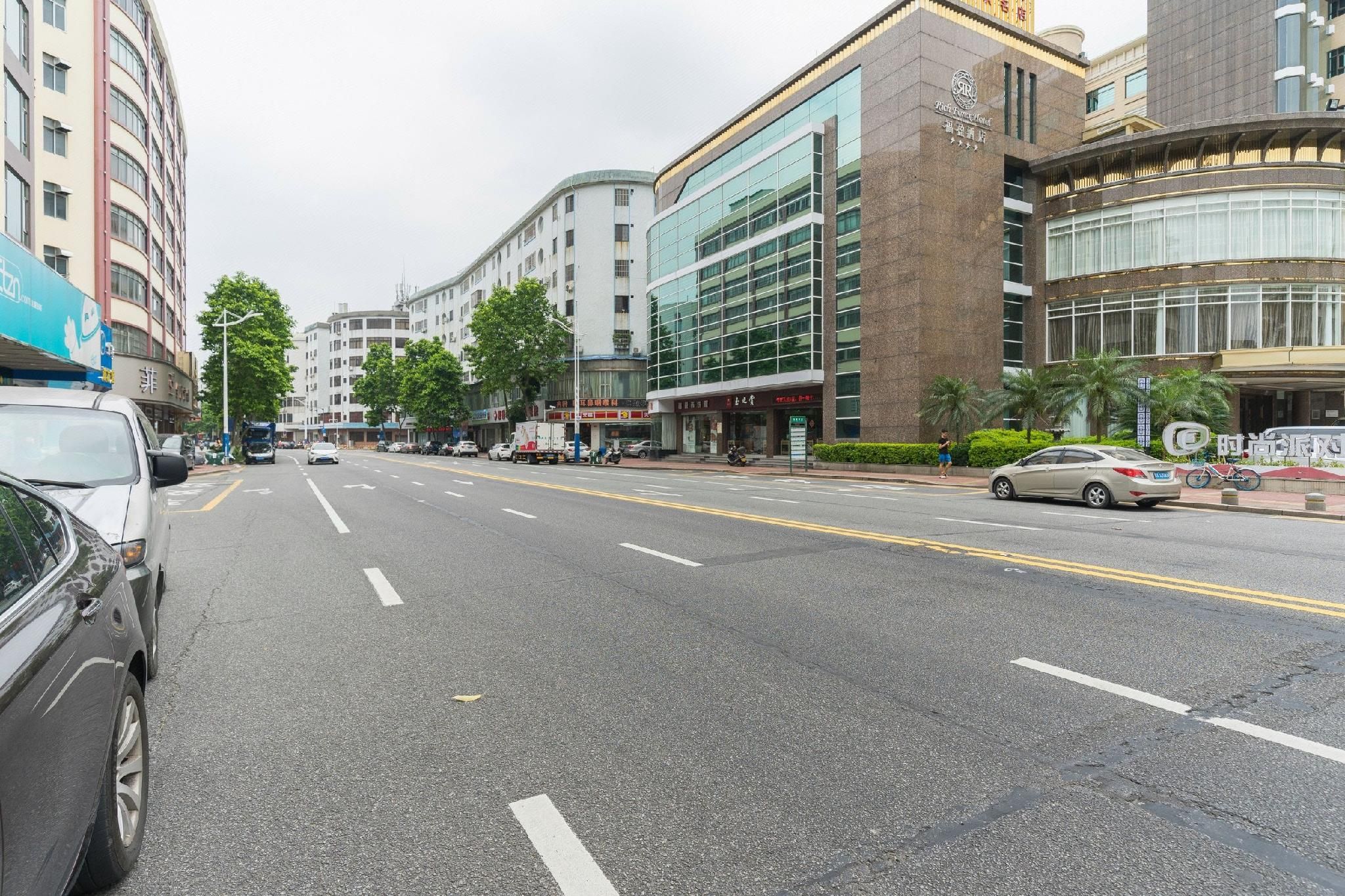 A multi-story hotel with a modern facade, a parking lot, and a street with vehicles and pedestrians.