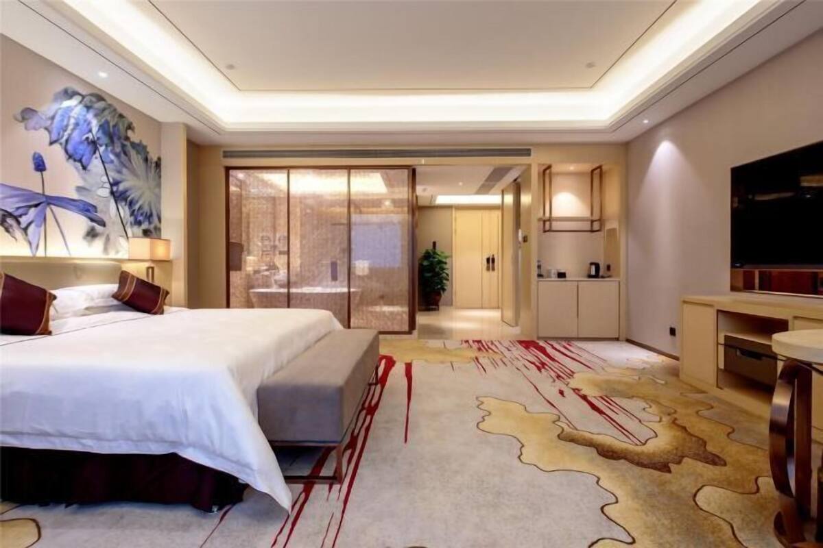 A modern hotel room with a large bed, a desk, a TV, and a sliding door leading to a bathroom.