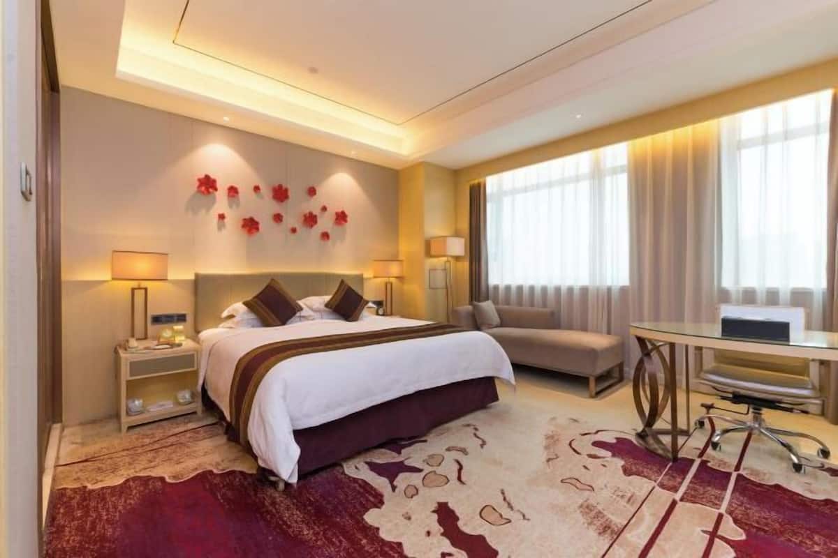 A hotel room with a bed, a sofa, a desk, and a large window with curtains.