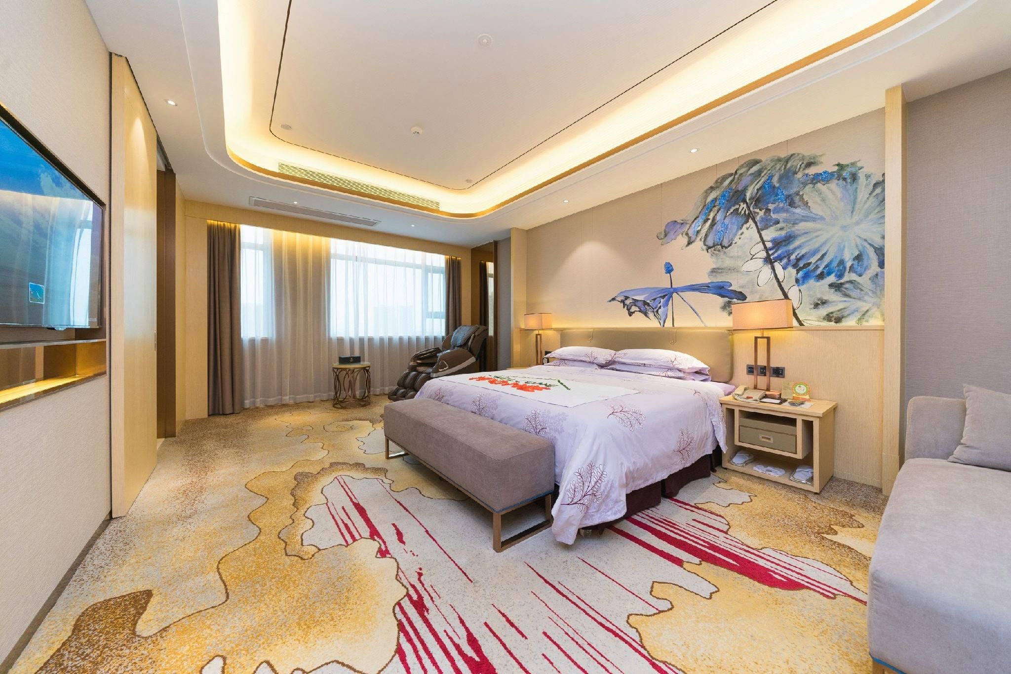 A hotel room with a large bed, a massage chair, a desk with a lamp, and a painting on the wall.