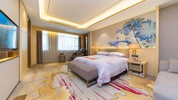 A hotel room with a large bed, a massage chair, a desk with a lamp, and a painting on the wall.