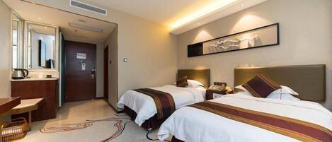 A hotel room with two beds, a desk, a mirror, and a wall-mounted artwork.