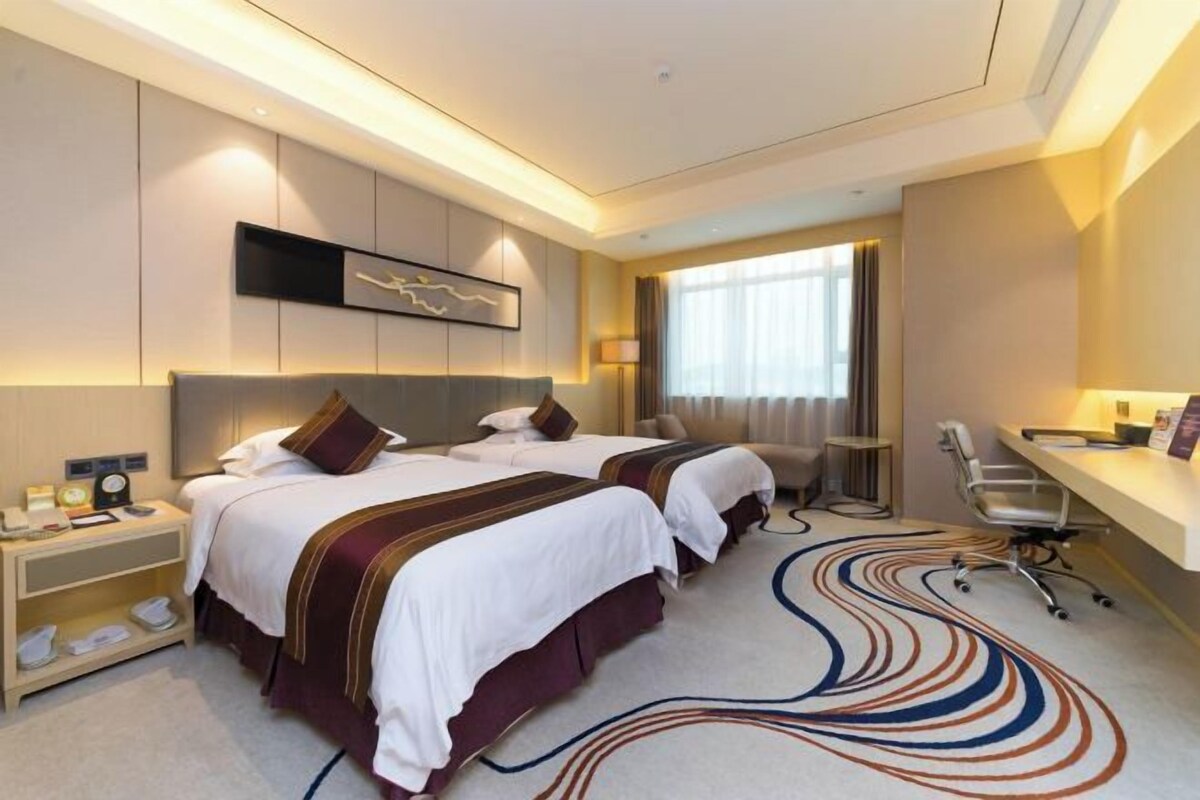 A hotel room with two beds, a desk, a chair, and a large window.