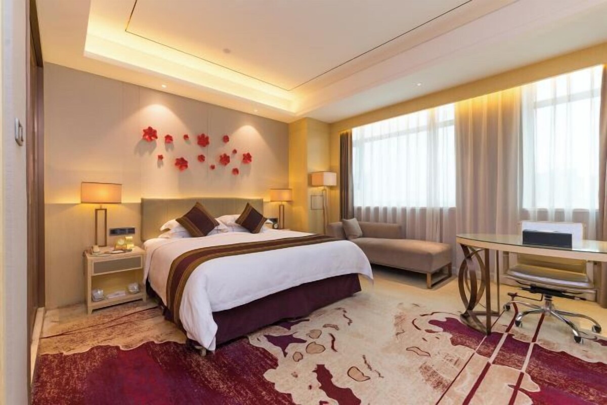 A hotel room with a bed, a sofa, a desk, and a large window with curtains.