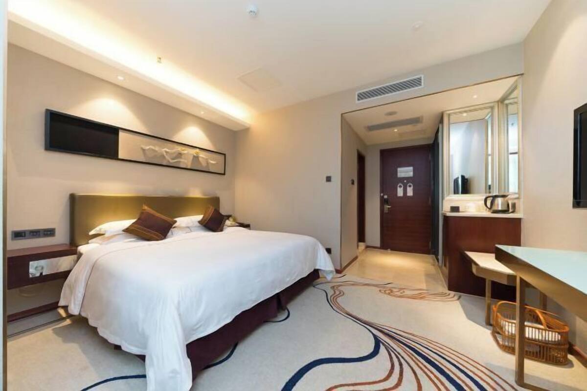 A modern hotel room with a large bed, bedside tables, a desk, and a mirror.