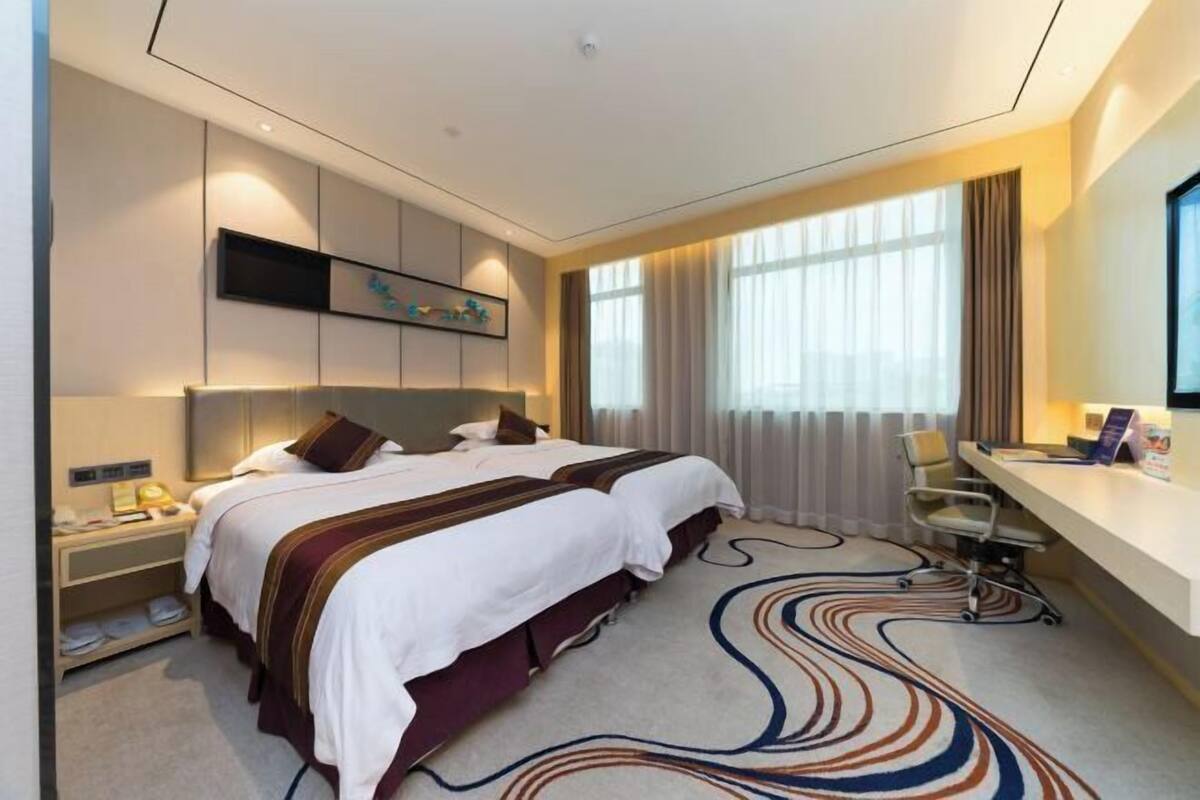 A hotel room with two beds, a desk, and a large window with curtains.