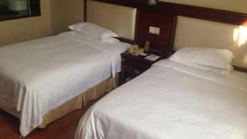 Quarto de hotel com duas camas de solteiro, cabeceira de madeira, mesa de cabeceira com telefone e luminária na parede.