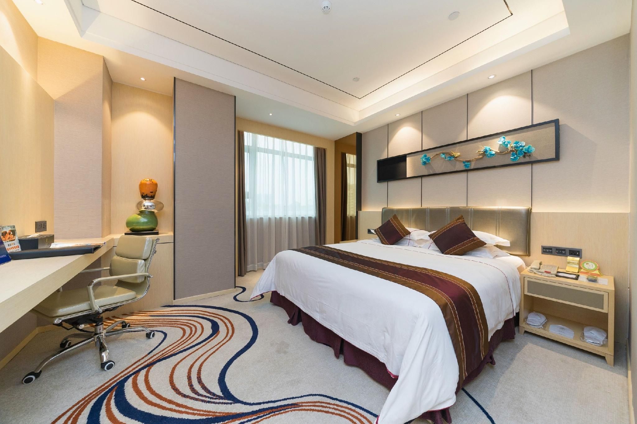 Une chambre d’hôtel avec un grand lit, un bureau, une chaise, une table de chevet et un élément décoratif mural.