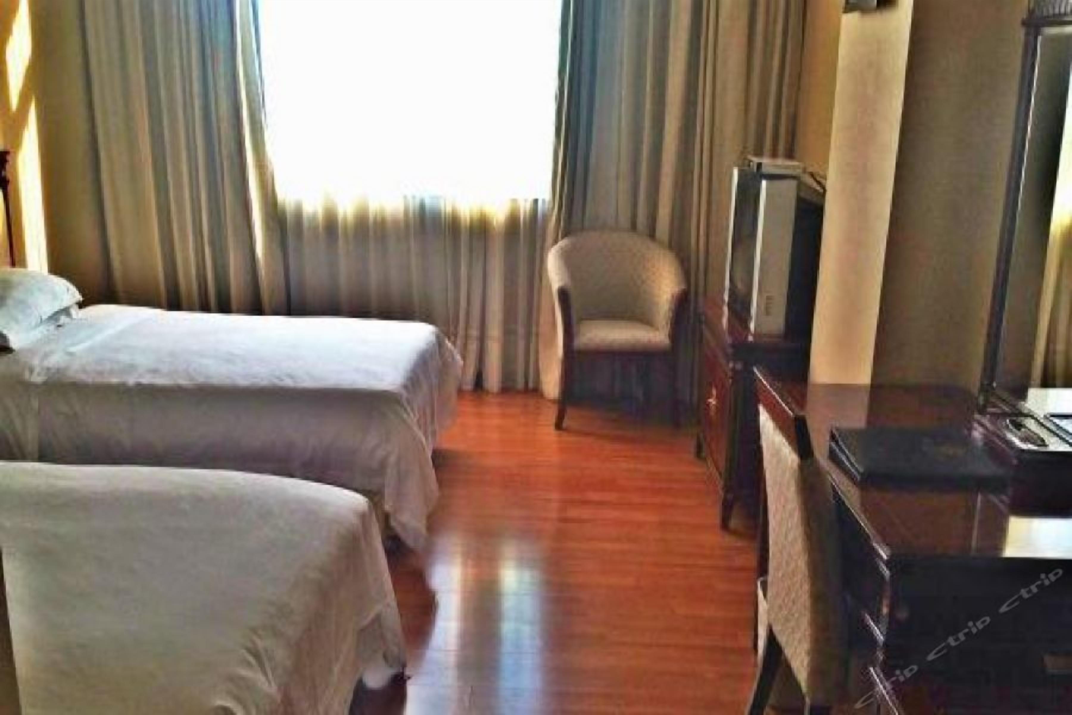 A hotel room with two beds, a chair, a desk, and a television.
