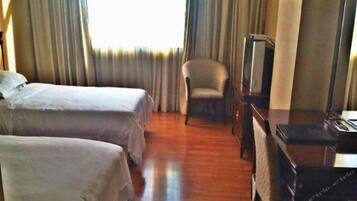 A hotel room with two beds, a chair, a desk, and a television.