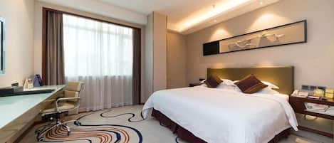 A hotel room with a bed, desk, chair, and a large window with curtains.