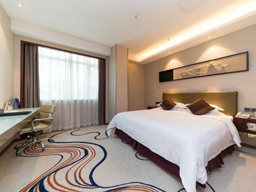 Habitación de hotel con cama, escritorio, silla y un ventanal con cortinas.