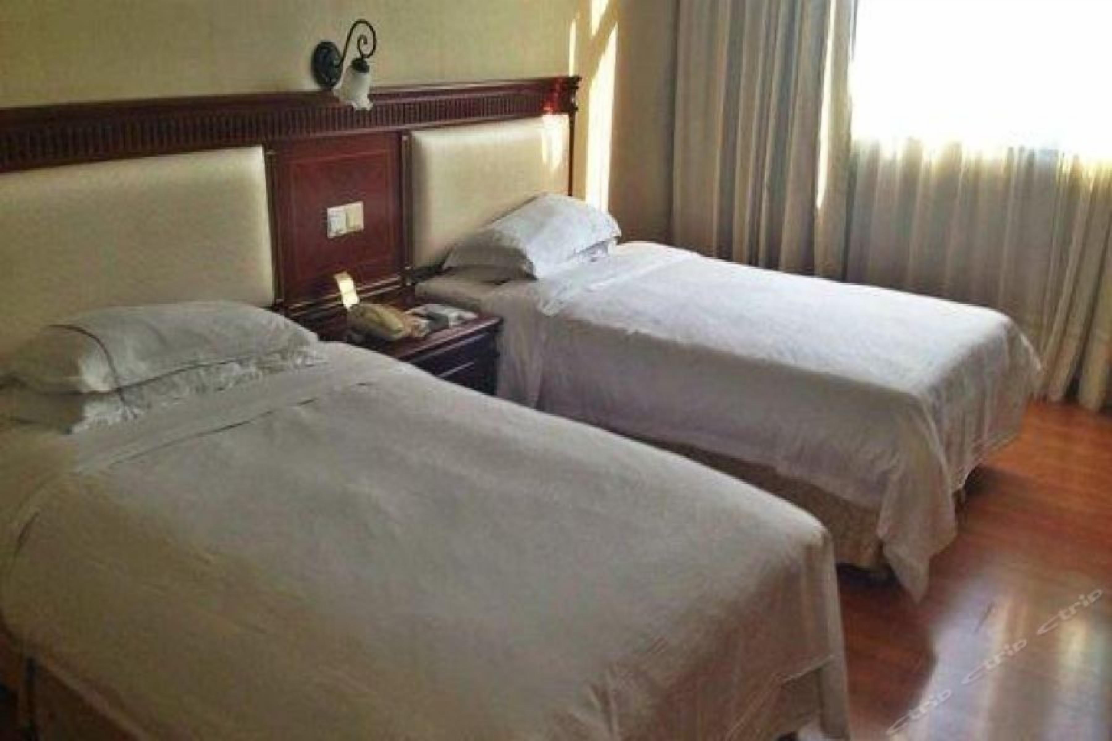 A hotel room with two beds, a nightstand, and a lamp.