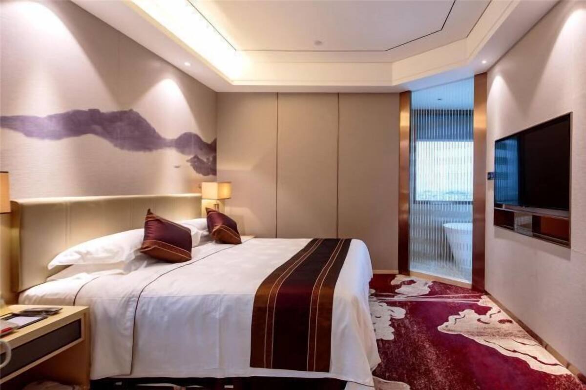 A hotel room with a bed, bedside tables, a TV, and a view through a window.