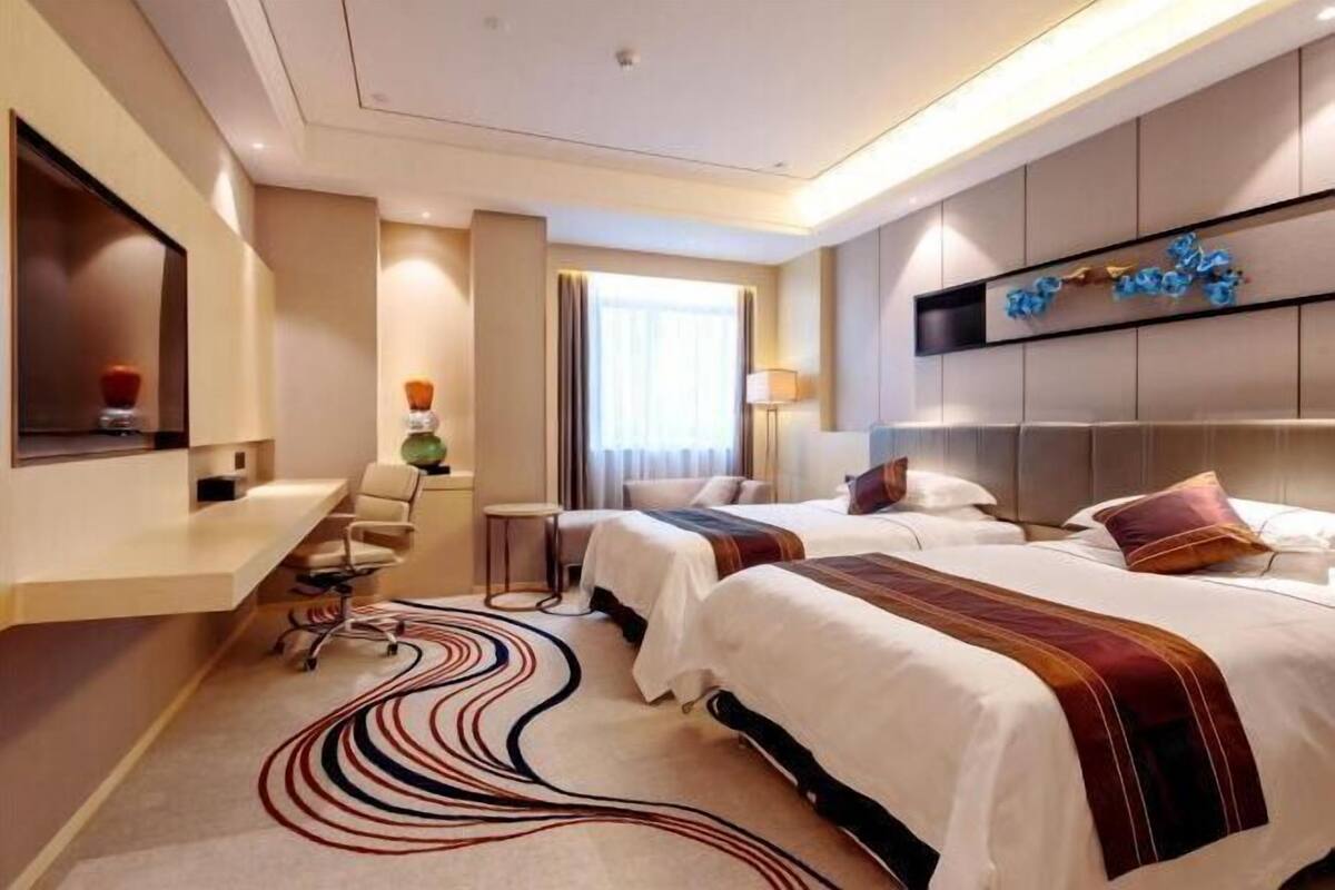 A hotel room with two beds, a desk, a chair, a lamp, and a decorative wall piece.