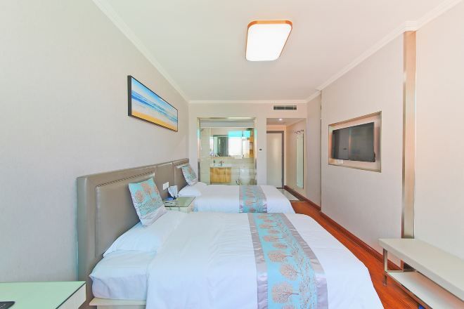 Habitación de hotel con dos camas, un televisor y un baño visible a través de una puerta de cristal.