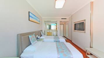 Habitación de hotel con dos camas, un televisor y un baño visible a través de una puerta de cristal.