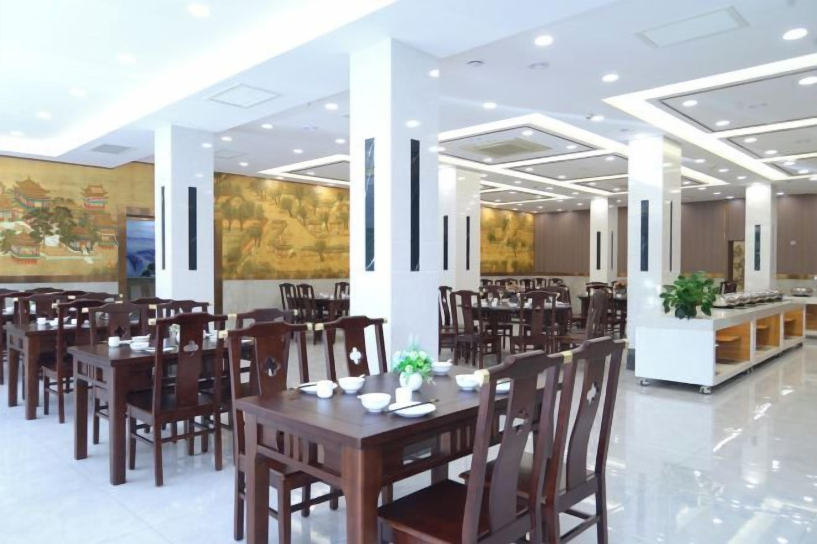 A spacious dining area with multiple tables and chairs, a central island with a plant, and a mural on the wall.