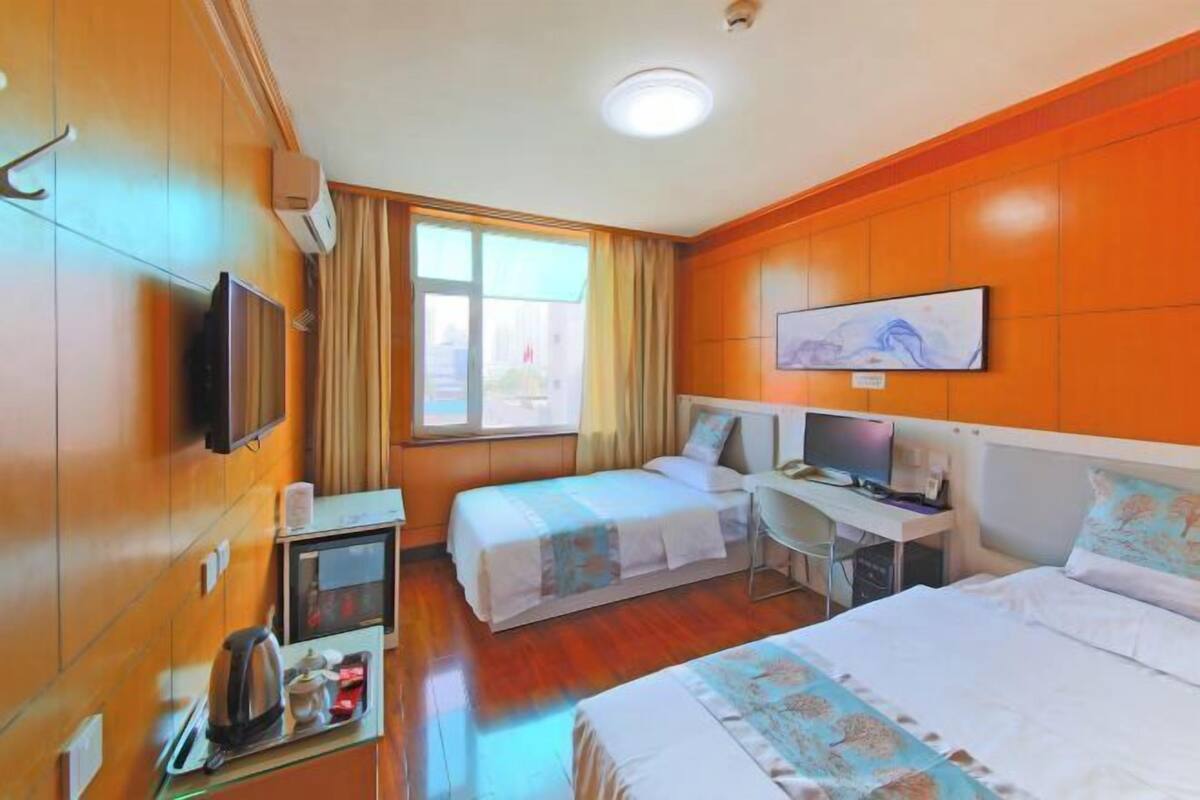 A hotel room with two beds, a desk, a television, and a window with curtains.