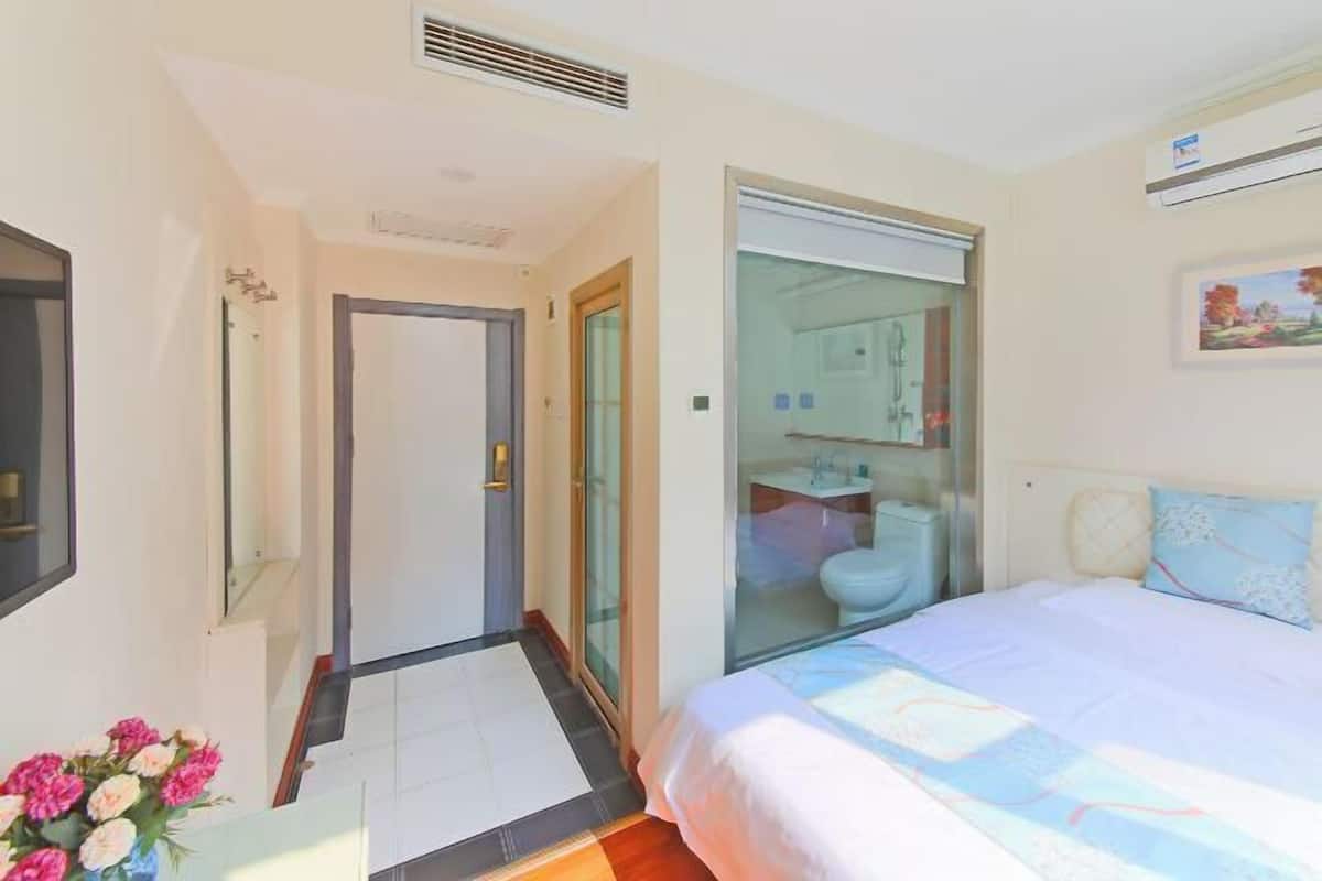 A bedroom with a bed, a bathroom with a glass door, and a hallway leading to another room.