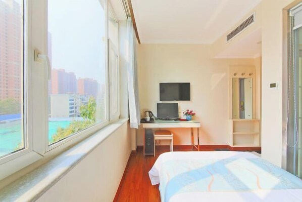 Una habitación de hotel con cama, escritorio con computadora, televisor y ventana con vista a la ciudad.