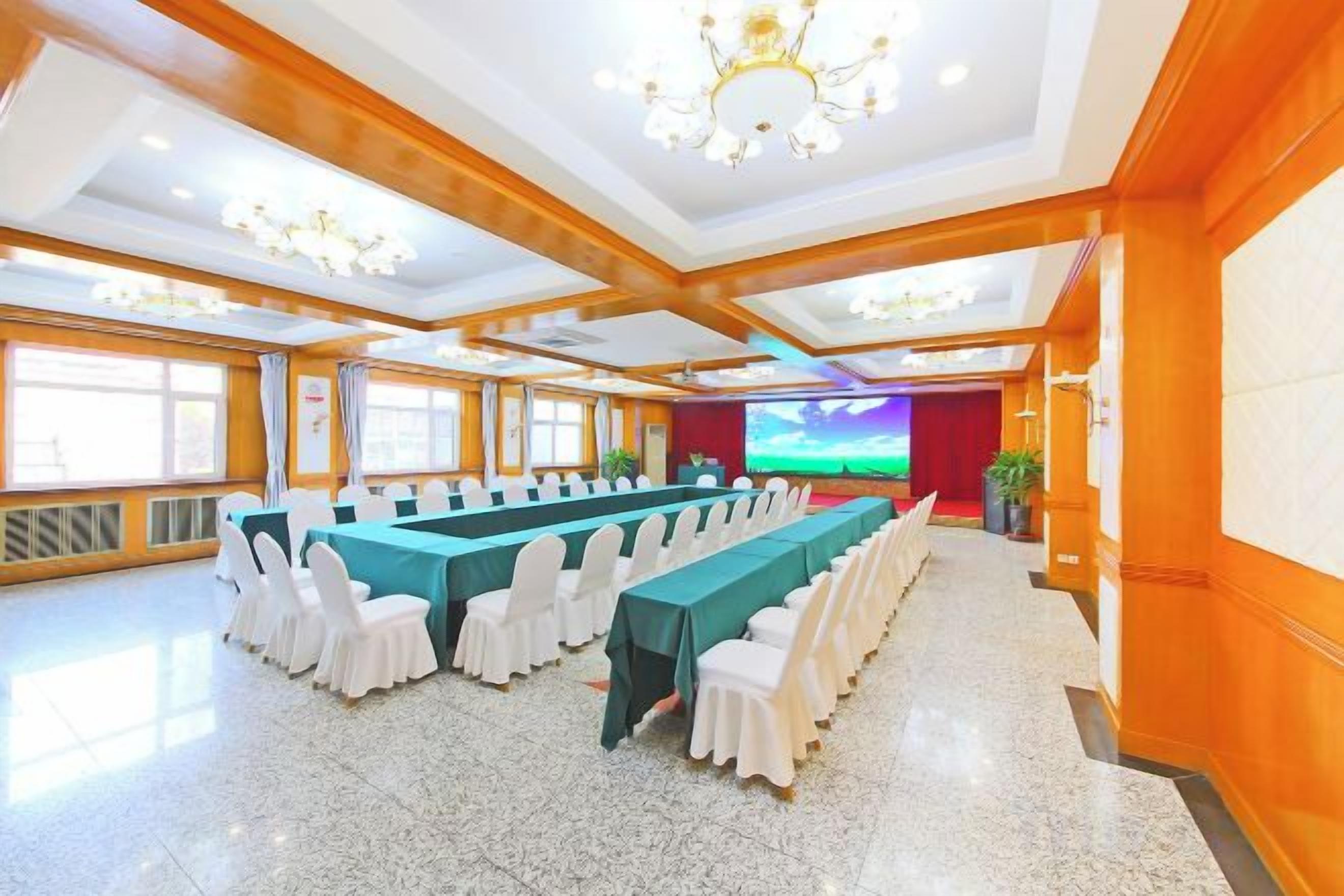 Uma sala de conferências com uma mesa comprida, cadeiras brancas e uma tela grande.