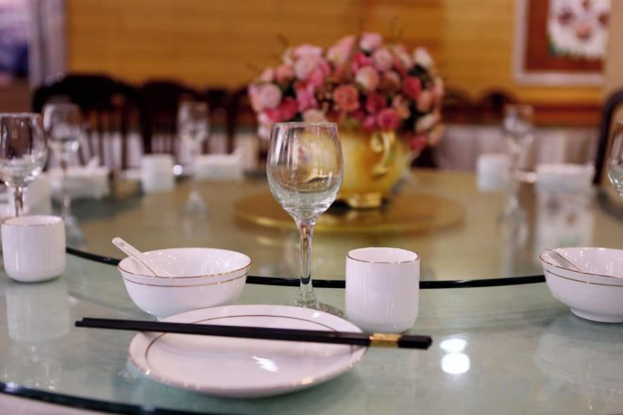 A table set with bowls, chopsticks, a wine glass, and a vase of flowers.