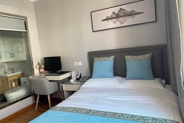Quarto de hotel com cama, escrivaninha com computador, televisão e banheiro com espelho e pia.