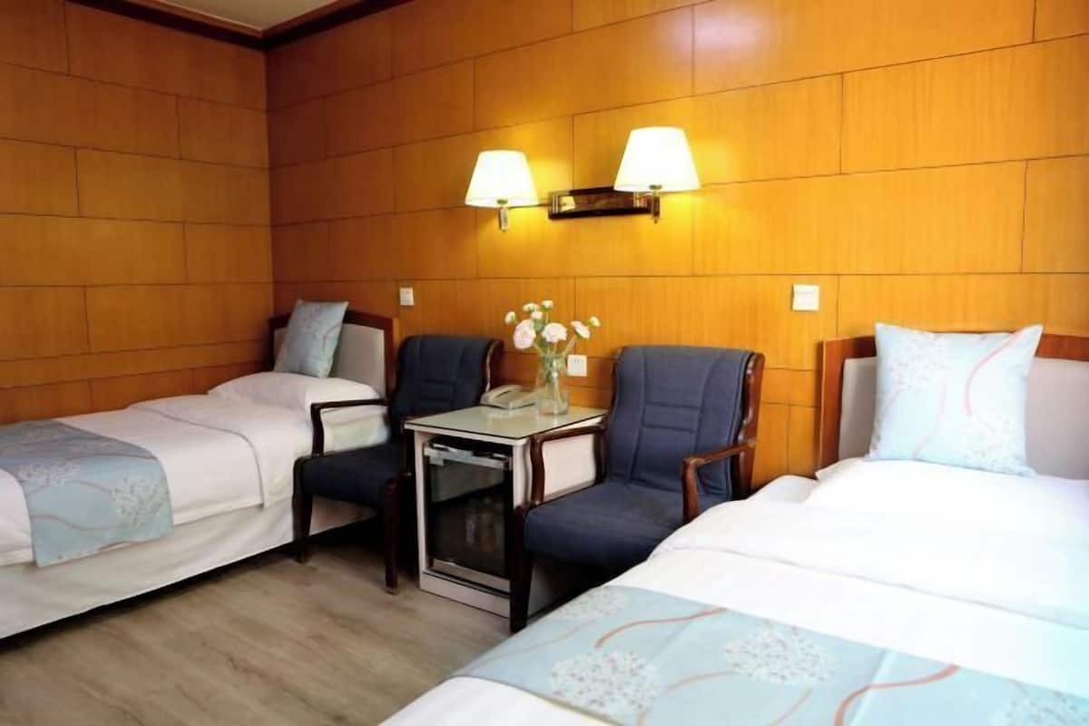 A hotel room with two single beds, a small table with a telephone, and two wall-mounted lamps.